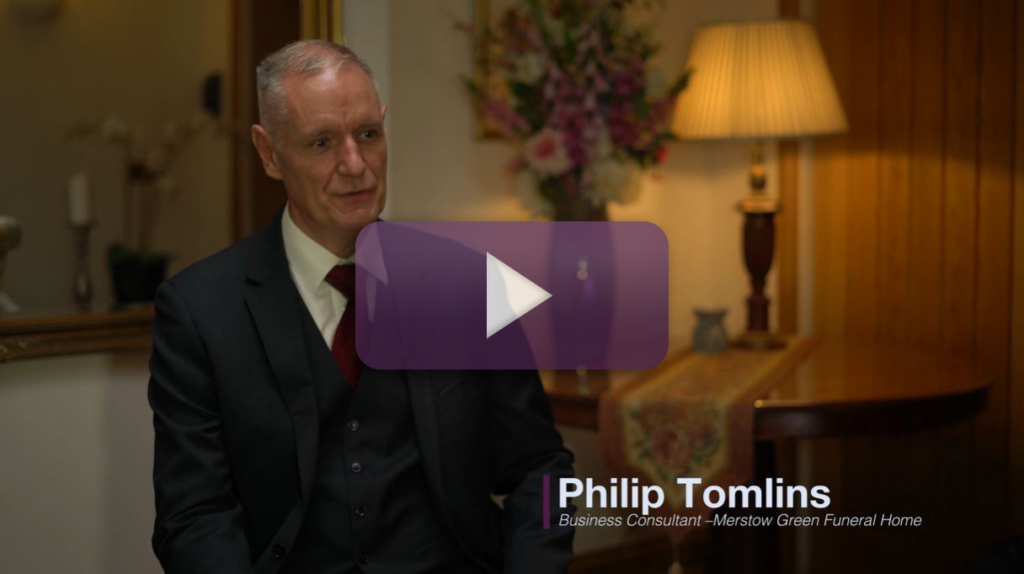 A still frame from a video featuring Phillip Tomlins of Merstow Green Funeral Homes with a play button in the centre of the frame.