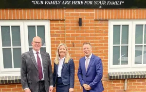 3 people in suits standing in front of brick wall for a picture.