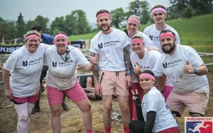 A team of 7 people posing for a photo covered in mud.